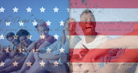Naklejka premium Sitting seven adults posing on sandy beach, wearing shorts shades, holding phone, flag overlay