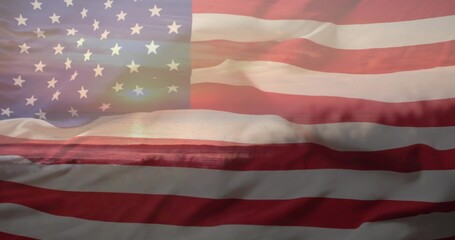 Waving American flag filling frame over coast, showing stars, stripes, folds, sun reflection