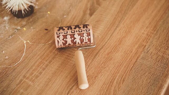 Gingerbread man dough roller with embossed figures and hearts on a wooden surface with festive lights.
