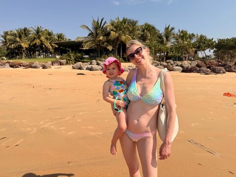 M&egrave;re tenant son enfant dans les bras sur une plage tropicale bord&eacute;e de palmiers
