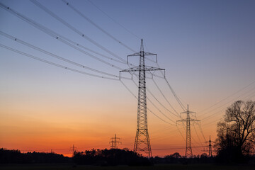 Strommasten und Hochspannungsleitungen in einer Landschaft bei Sonnenuntergang als Symbolbild f&uuml;r Stromnetz, Energiewende und den Ausbau der Energieinfrastruktur. 