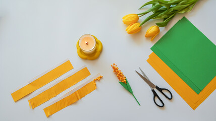 DIY spring craft project with yellow tulips, paper, scissors, and a lit candle