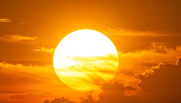 A bright sun sets behind dark orange clouds in the sky