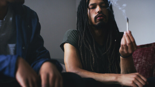 Smoking, home and people with weed on sofa for social hangout, relax and bad habit on weekend. House, friends and men in living room with joint or cannabis for addiction, risk and unhealthy influence