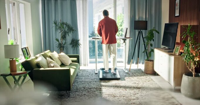 Man, standing desk and treadmill in lounge with remote work from home for fitness, multitask and project. Person, freelance writer and exercise with notes, cardio and back in living room at apartment