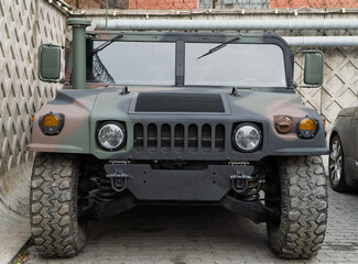 Obraz premium Military Humvee parked on an street, showcasing its rugged design and operational readiness in a secure military base. Khaki camouflage military Hummer front view. HMMWV.
