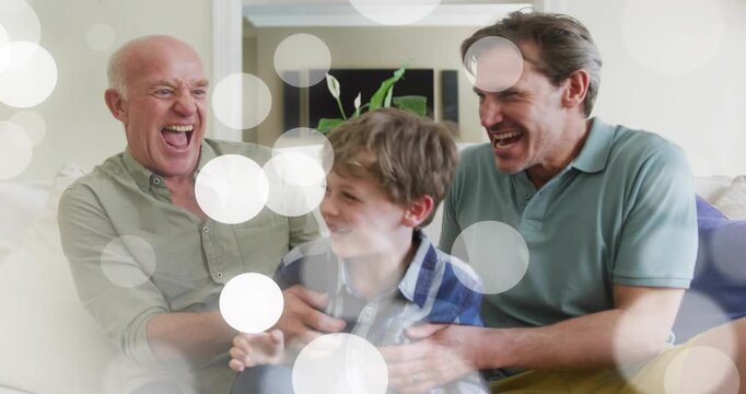 Granddad and dad tickling boy after boy leaning on sofa, family fun, bokeh drifting over trio