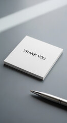 White square paper with Thank You text and silver pen on gray surface, representing gratitude, appreciation and business correspondence concept