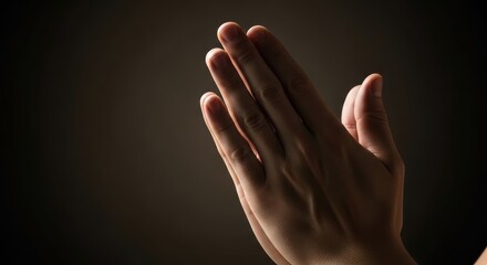 Close-up of praying hands in soft light, conveying hope and spirituality against a dark background.