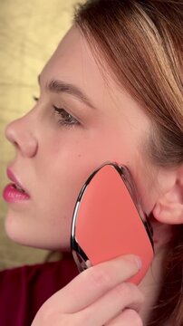 A young woman enjoys a facial massage with a microcurrent massager. Professional body treatment. Wrinkle smoothing.