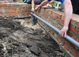 Obraz premium Plumbers Installing Sewer Drain Pipe in House Foundation