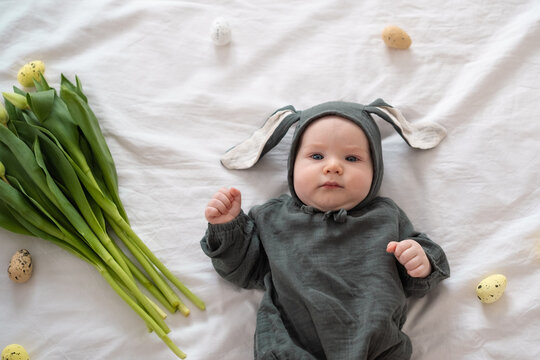 A cute little boy in a bunny costume holds a bouquet of tulips on a spring day. Funny kid on Easter