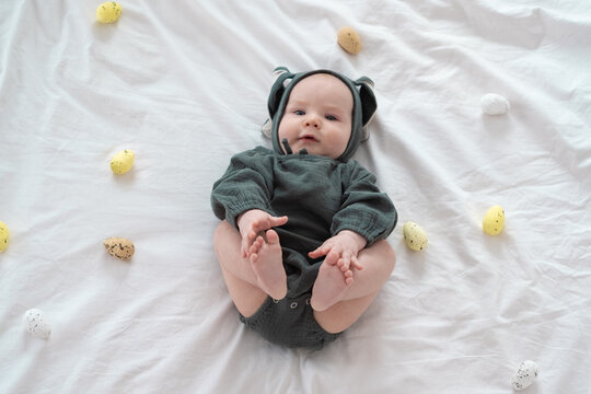 A cute boy in a bunny costume plays with colorful Easter eggs on a spring day. Funny child on Easter.
