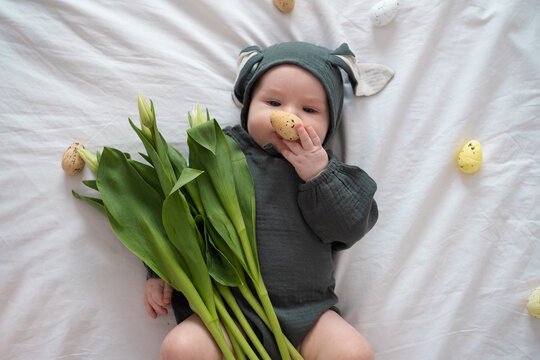 A cute little boy in a bunny costume holds a bouquet of tulips on a spring day. Funny kid on Easter