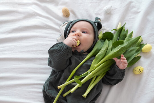 A cute little boy in a bunny costume holds a bouquet of tulips on a spring day. Funny kid on Easter