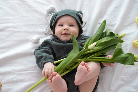 A cute little boy in a bunny costume holds a bouquet of tulips on a spring day. Funny kid on Easter