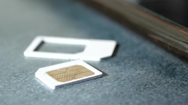 Close up of a SIM card and adapter tray on a gray surface with smartphone edge in background, showcasing telecommunication technology