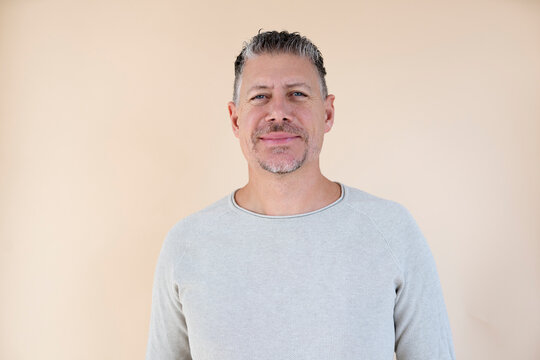 Man with gray hair and brown sweater standing in front of brown background