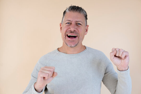 Man with gray hair and brown sweater standing in front of brown background