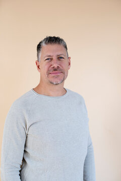 Man with gray hair and brown sweater standing in front of brown background