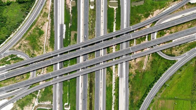 Aerial view of modern highway interchange with multilayer roads and curved ramps surrounded by green farmland, showcasing transportation infrastructure, urban development, and road network planning.