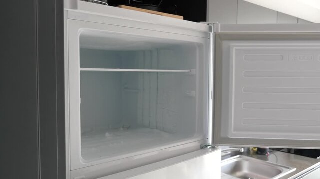 Opening refrigerator door reveals an empty freezer covered in frost, suggesting need for defrosting