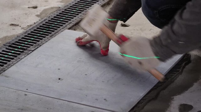 Professional builder worker installing floor a large ceramic tile at repair renovation work using a laser level. Man experienced repairman laying placing tile indoors house or apartment. Worker. 