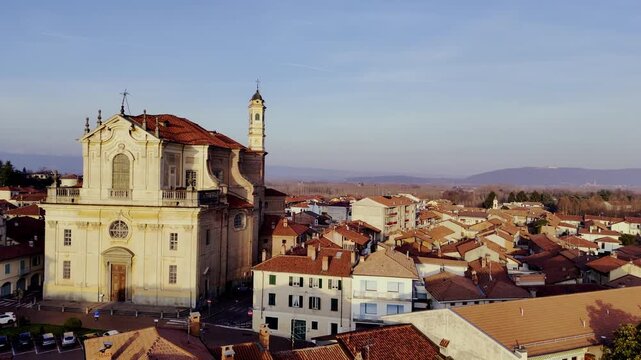 STRAMBINO, ITALY - FEBRUARY 24, 2026: Aerial drone footage starting from behind the historic Chiesa Parrocchiale dei Santi Michele e Solutore, sliding laterally to reveal the side elevation of the bui