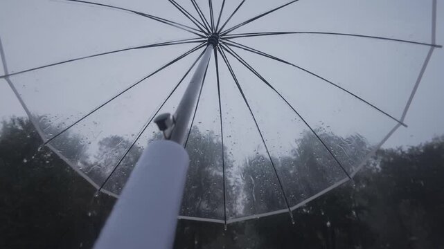 Slow motion of raindrops falling on transparent umbrella canopy, POV shot. Walk with tranparent parasol overhead during downpour, drops flow down its clear dome, first-person view from below
