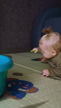 Small kid with a shovel in hands lies on the floor. A blue washtub is near the infant. Vertical video