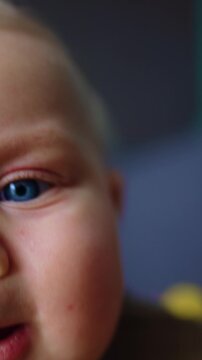 Chubby face of a cute Caucasian blue-eyed baby. Close up. Curious infant trying to get a camera. Vertical video