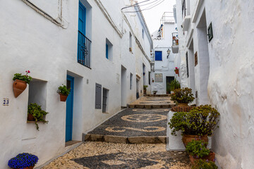 Fototapeta premium One of the picturesque streets of Frigiliana, a white Andalusian village, with whitewashed facades decorated with potted plants and flowers, and traditional mosaic floors. Málaga, Spain