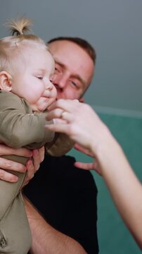 Father holds a cute little baby in hands. Mother entertains the child and kid is smiling adorably. Low angle view. Vertical video