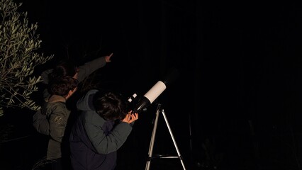 Learning about planets and stars in the deep night sky, two children stargazing with a telescope, discovering astronomy and cosmic wonders together outdoors © DawDunia