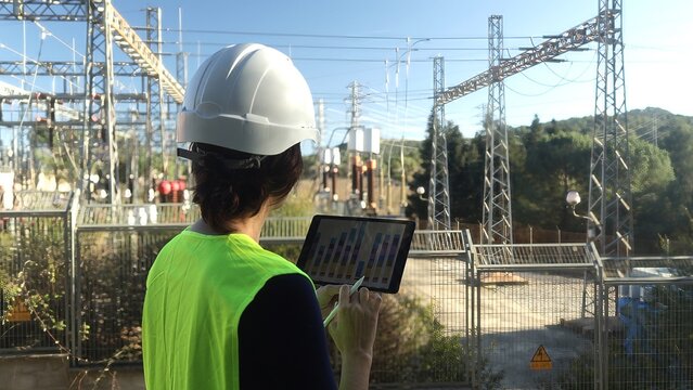 Electrical engineer using a tablet for data analysis and monitoring the power grid at an outdoor high voltage electricity substation