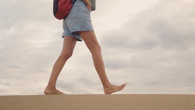 Woman with a backpack walking barefoot on sand dunes, experiencing freedom and connection with nature during an outdoor travel adventure, enjoying the desert landscape