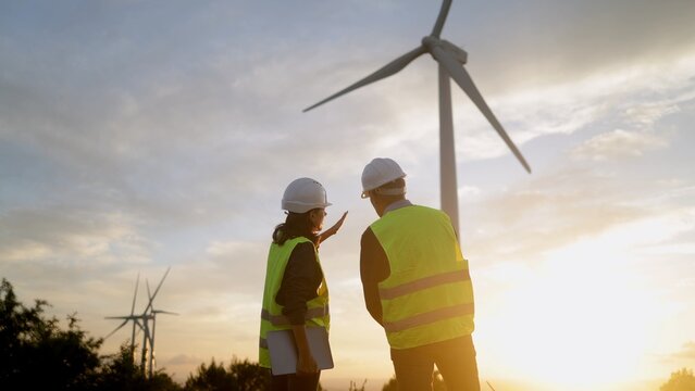 Engineers discussing wind power generation at a wind farm during sunset, focusing on sustainable energy solutions and renewable electricity development