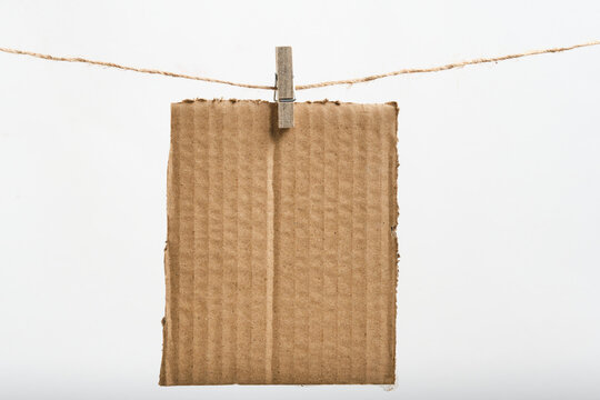 Piece textured brown cardboard hanging from twine string with wooden clothespin.