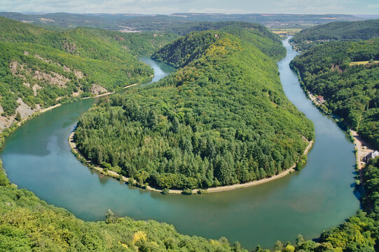 Panorama of the Saar Loop near Orscholz. The river winds in a striking curve through the dense, green forest under a blue summer sky. Top view.