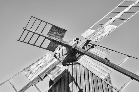Historic wooden windmill in a rural meadow, surrounded by fields and trees, creating an idyllic, tranquil landscape. In black and white.