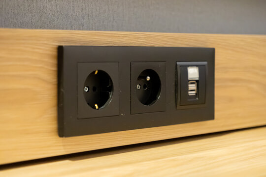 Black integrated power outlet with two sockets and a USB port on a wooden panel, providing convenient charging for modern interiors