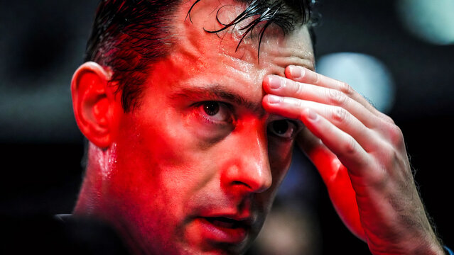 A man intensely focuses, forehead flushed red, hand pressed to his temple. He appears stressed and contemplative.