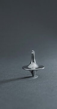 Metallic Spinning Top Falling Over. Linear footage of a shiny chrome top in steady rotation, progressively wobbling with increasing tilt until it fully topples on a matte gray surface.
