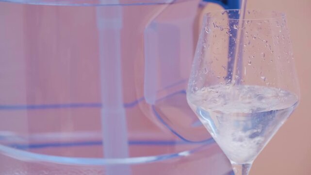 Water pouring into glass from tap or pump with bottled clean drinking water in background freshness and home hydration