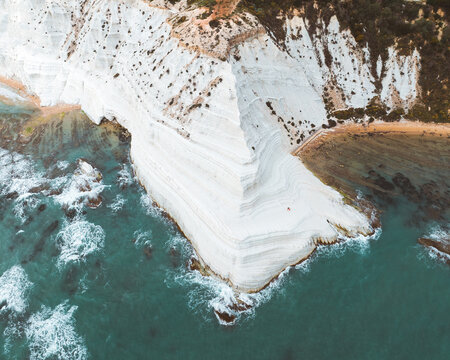Aerial view of the dazzling white cliffs of Scala dei Turchi descend into the turquoise embrace of the sea, a stark contrast against the rugged coastline, Agrigento, Sicily, Italy.