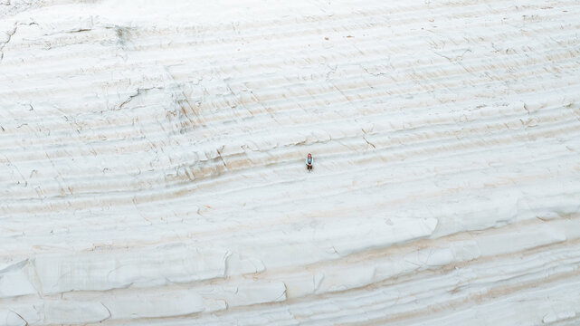 Aerial view of a lone figure stands on the Scala dei Turchi, its white cliffs contrasting against the azure sky, Agrigento, Sicily, Italy.