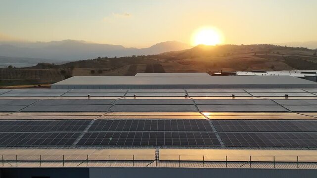 Aerial view of solar panels on industrial warehouse rooftop at sunset. 