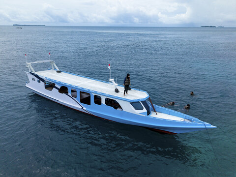 Aerial view of a white and blue boat on the turquoise sea with people snorkeling near Cemara Kecil, Karimunjawa, Central Java, Indonesia.
