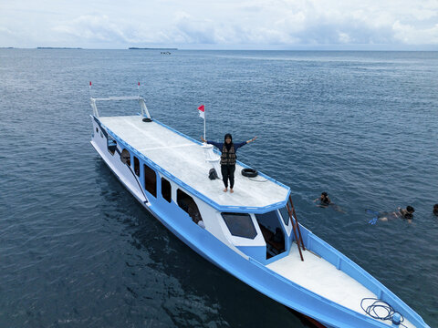 Aerial view of a boat with a person standing on top with swimmers nearby, Cemara Kecil Snorkeling Spot, Karimunjawa, Central Java, Indonesia.