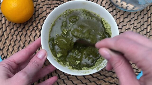 Female hands mix henna powder with water and stir with spoon for hair dye preparation closeup